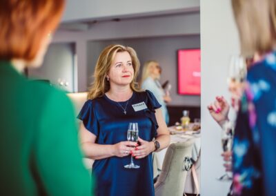 a woman in a blue dress holding a glass of prosecco and listening networking